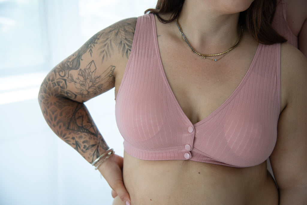 Vrouw met tattoos op linkerarm draagt roze voedingsbeha met 3 drukknoopjes aan de voorkant